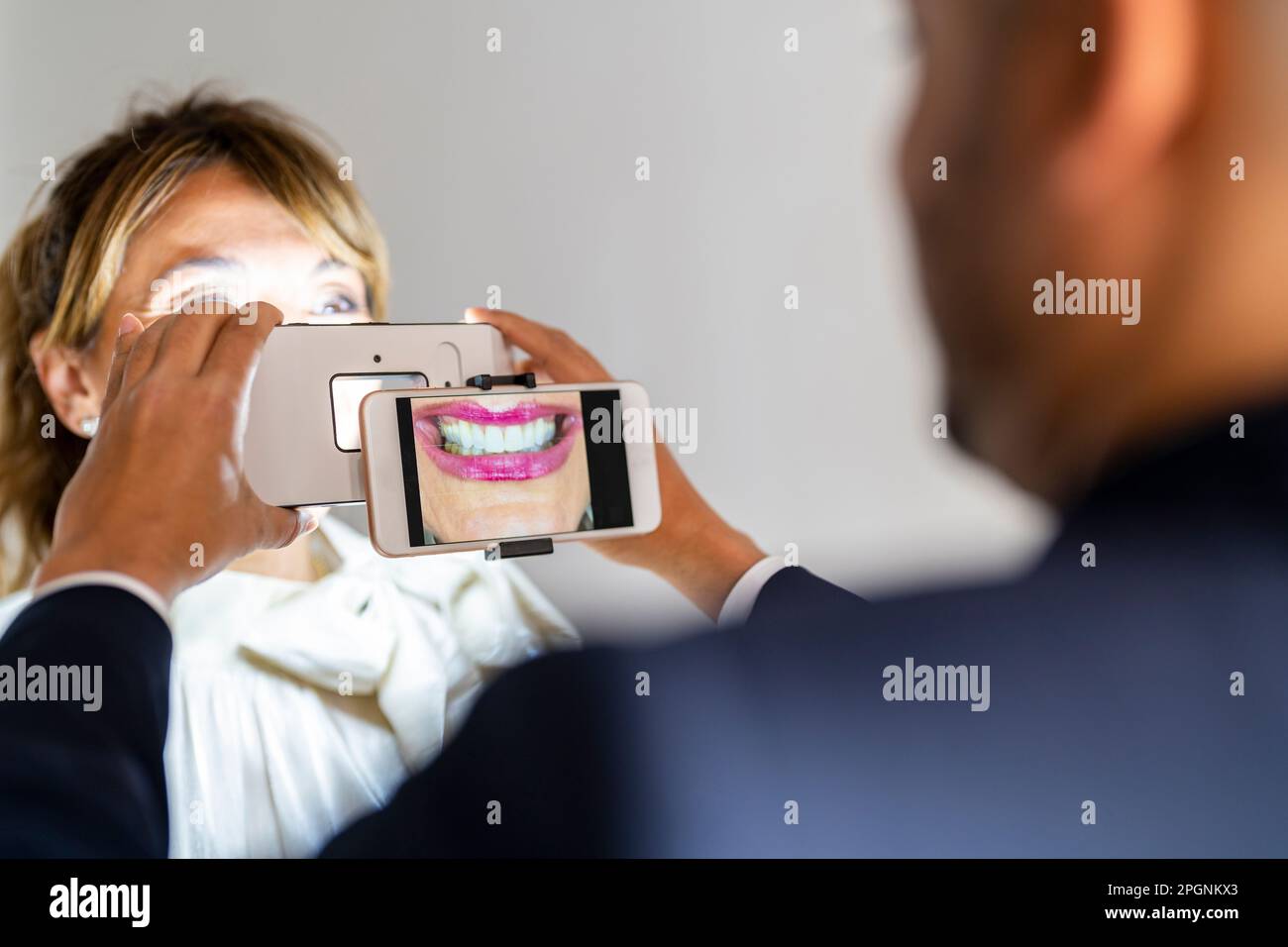 Geschäftsmann, der das Lächeln eines Kollegen mit einem Smartphone fotografiert, mit Vergrößerungsgeräten Stockfoto