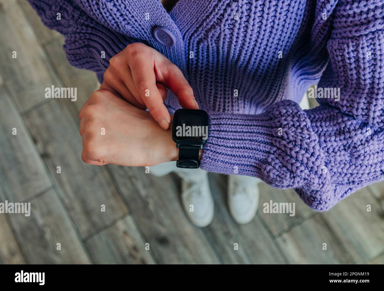 Eine Frau, die einen lila Pullover trägt und die Zeit auf der Smartwatch überprüft Stockfoto