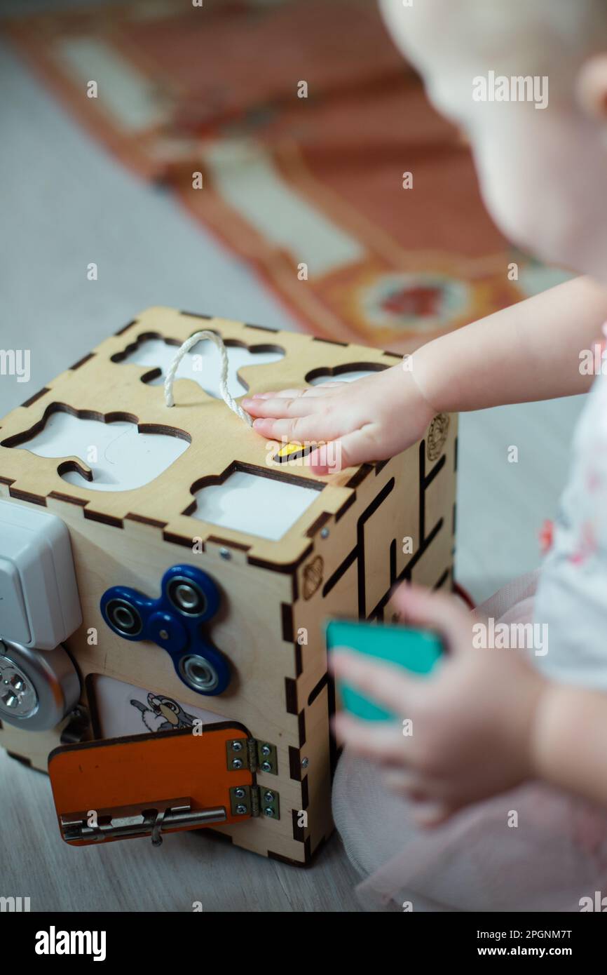 Sensorische Tafel. Ein Kind versucht, eine Figur für einen Sortierer in einem ausgelasteten Würfel zu finden. Ein Spielzeug zur Verbesserung der Farb- und Formerkennung. Pädagogisches Holz Stockfoto