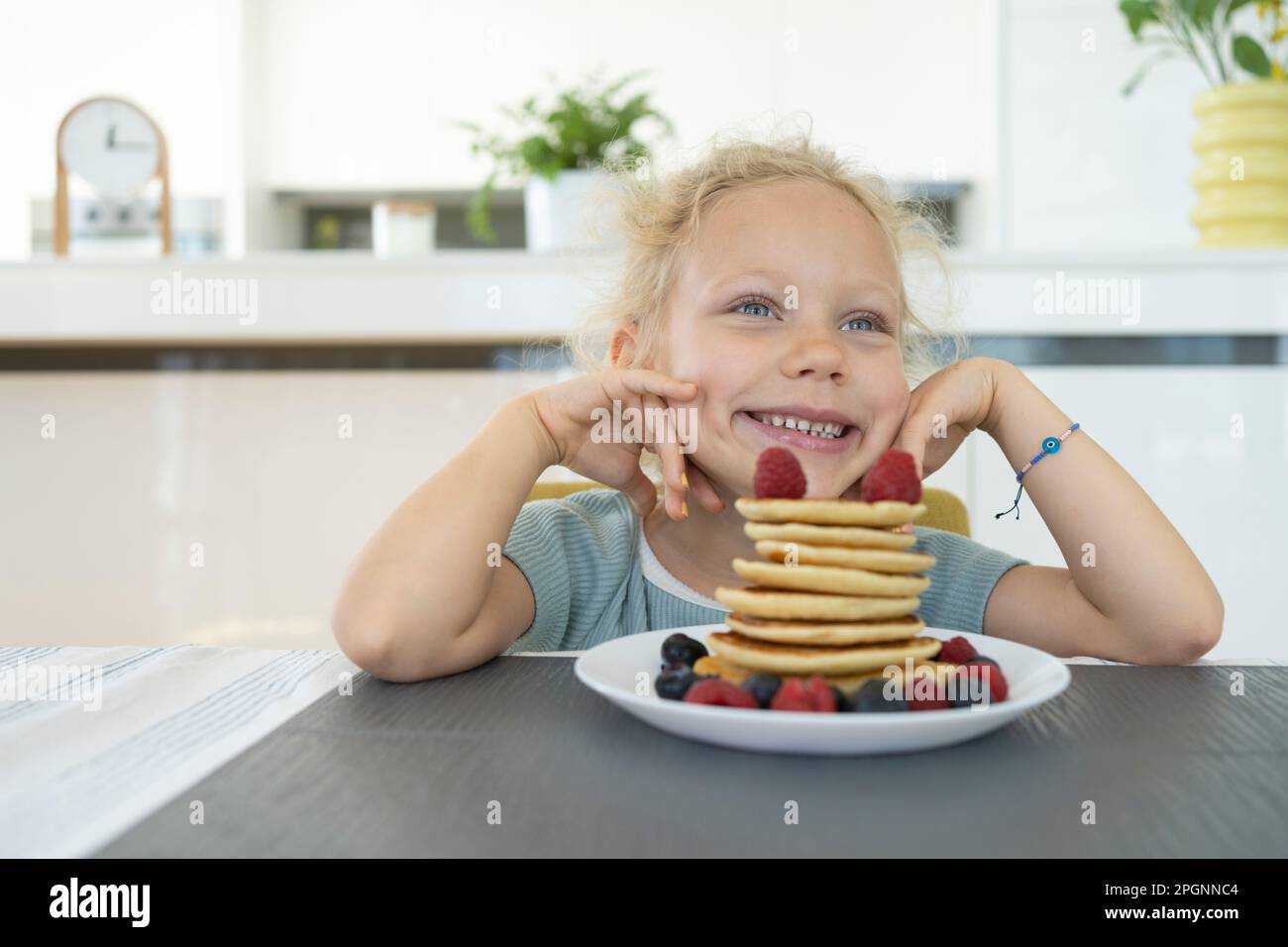 Lächelnder Mädchentag, träumt von einem Teller frischer Pfannkuchen zu Hause Stockfoto