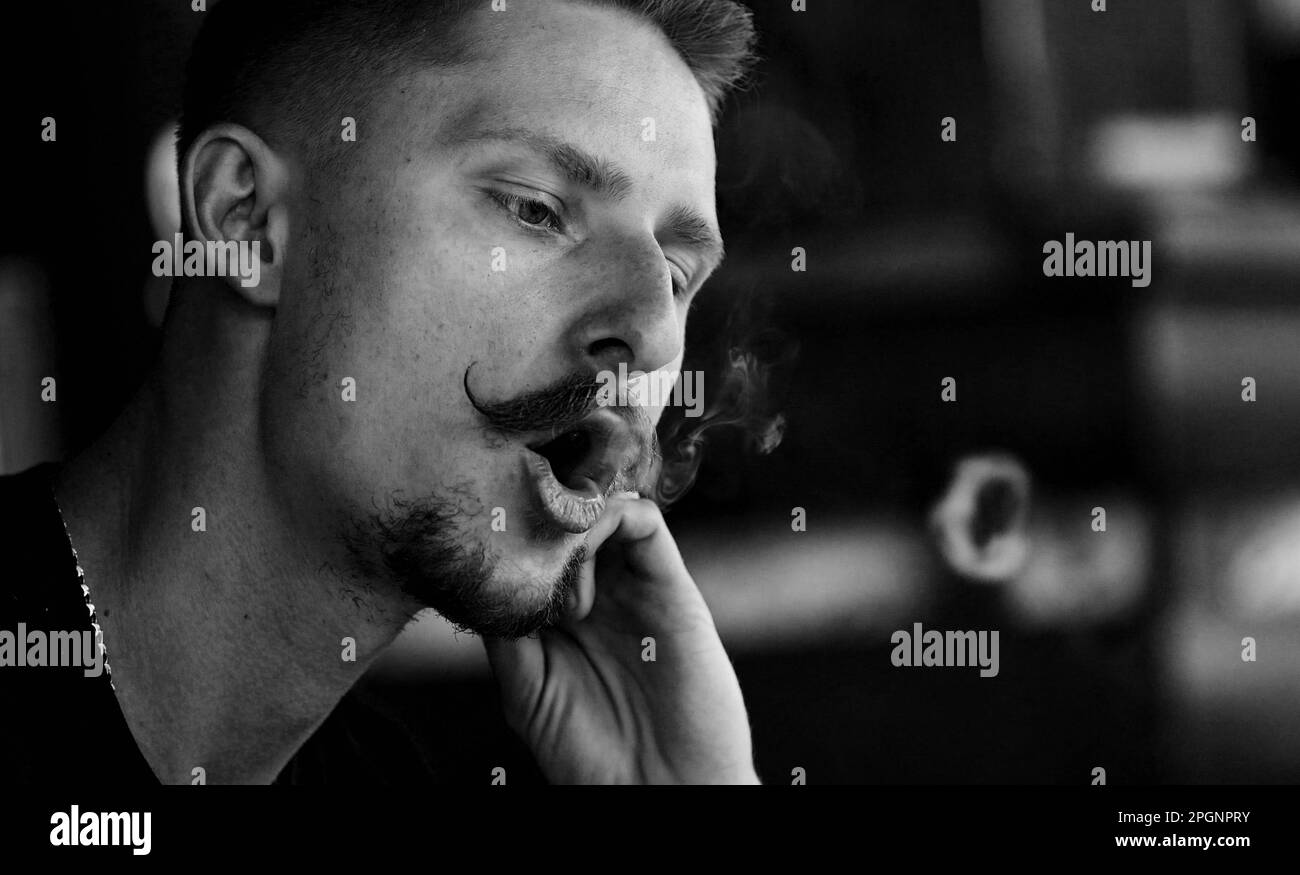 Hübscher junger Mann mit Bart und Schnurrbart, der eine elektronische Zigarette dampft. Hipster-Typ, der Smoke Rings ausatmet Stockfoto