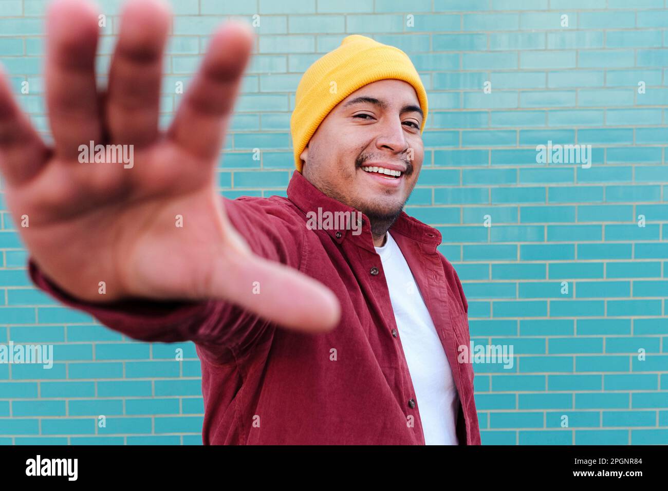 Ein glücklicher Mann hört auf, vor einer türkisfarbenen Ziegelwand zu Gesten Stockfoto
