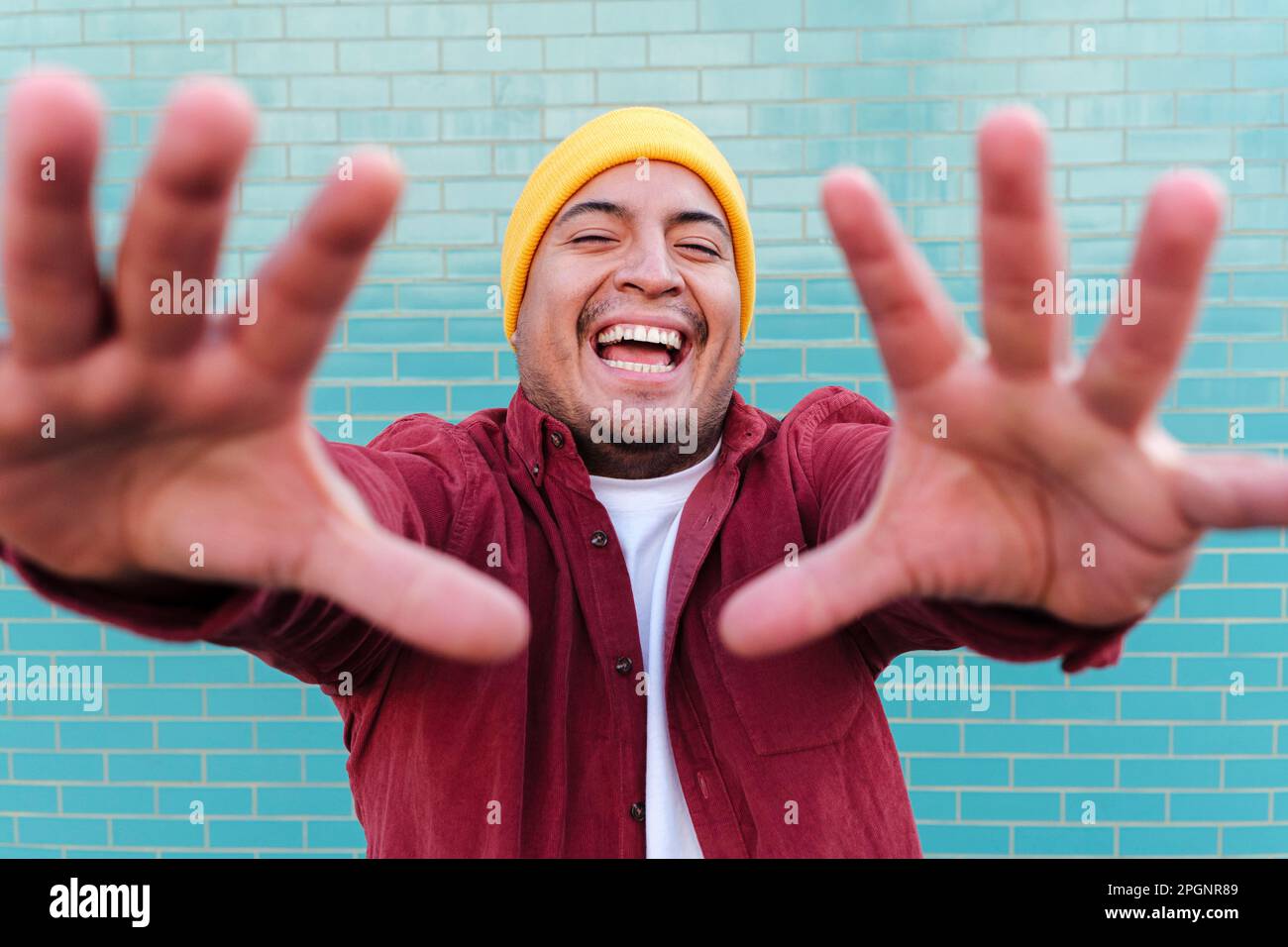 Fröhlicher Mann, hör auf, vor der türkisfarbenen Ziegelwand zu Gesten Stockfoto