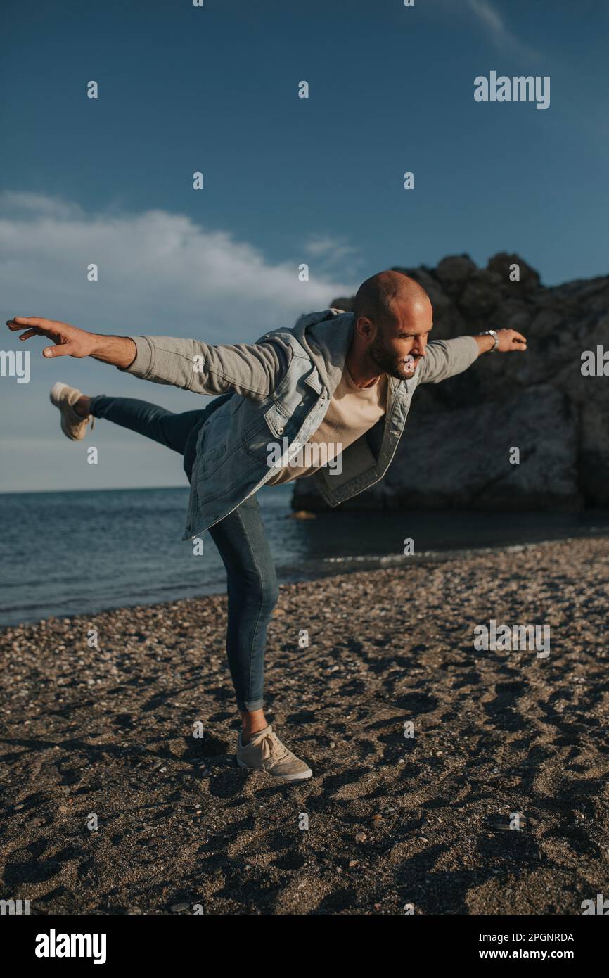 Ein Mann balanciert am Strand auf einem Bein Stockfoto