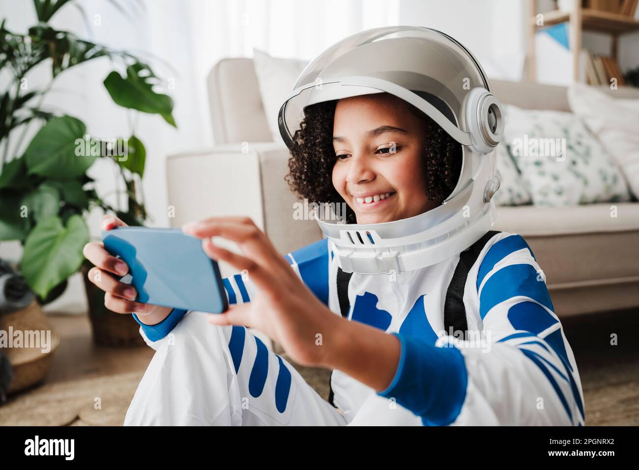 Mädchen, die einen Raumanzug trägt und zu Hause ein Smartphone benutzt Stockfoto