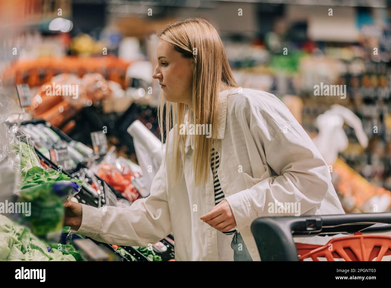 Eine Frau mit blonden Haaren, die Gemüse im Supermarkt aufsammelt Stockfoto