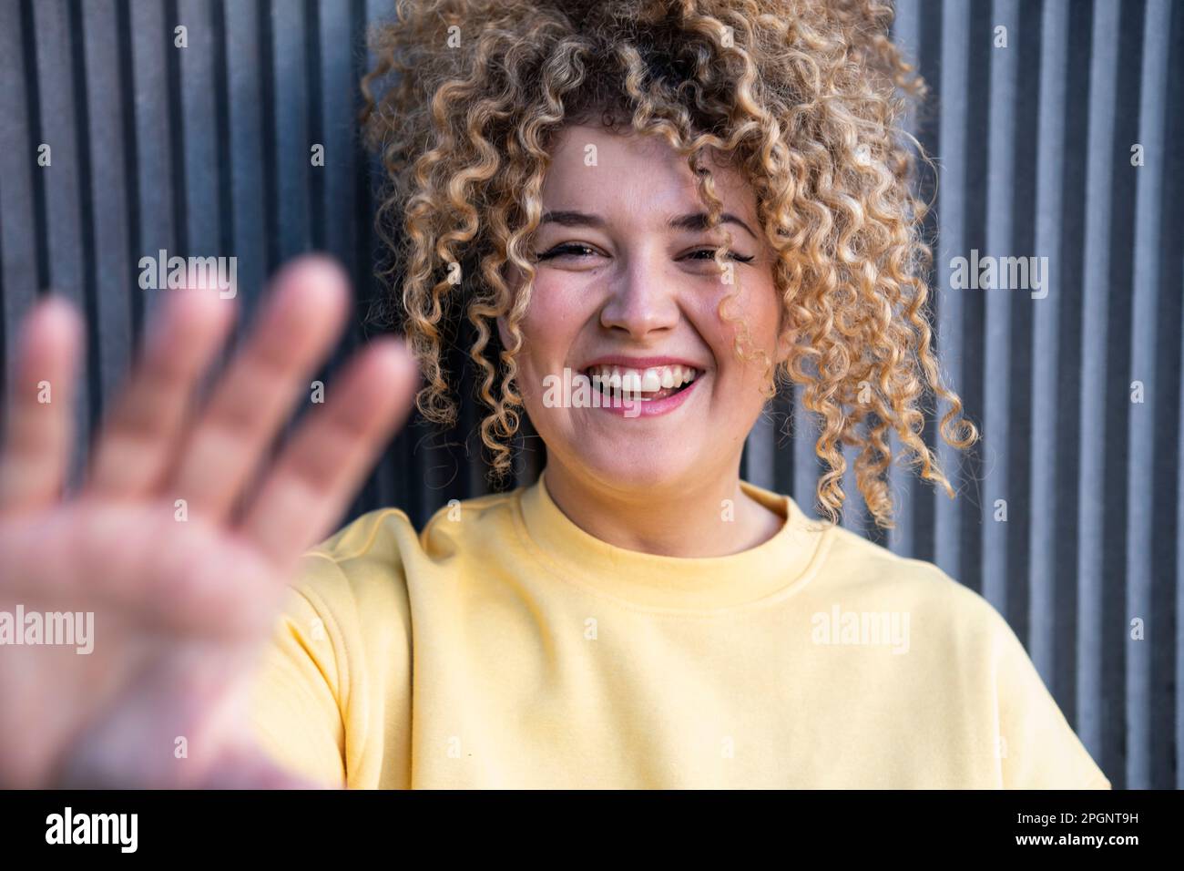Glückliche junge Frau, die vor der Wand eine Stoppbewegung zeigt Stockfoto