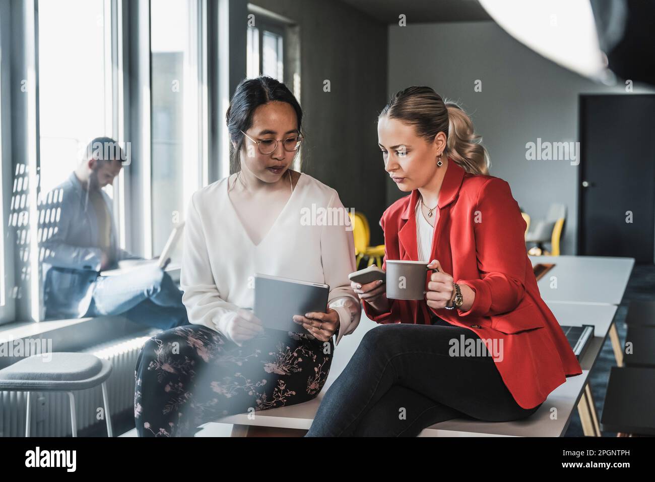 Geschäftsfrauen, die drahtlose Technologien verwenden, sitzen am Schreibtisch im Büro Stockfoto
