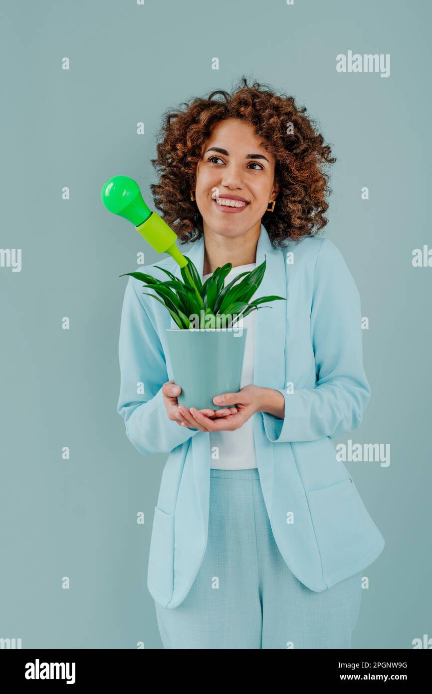 Rücksichtsvolle Frau mit grüner Glühbirne in Topfpflanzen vor blauem Hintergrund Stockfoto