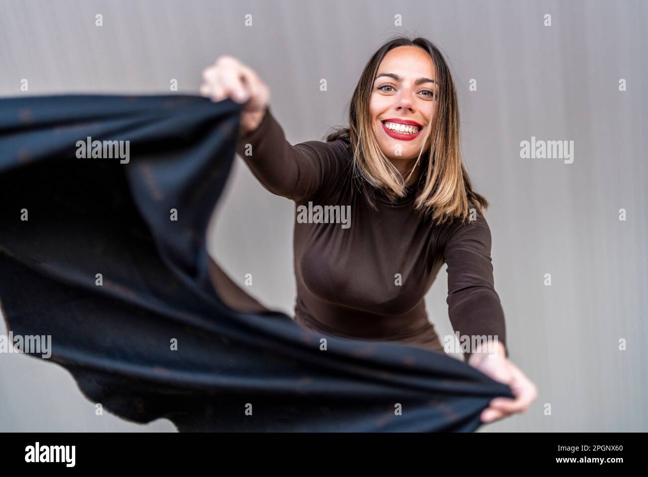 Glückliche Frau, die vor der grauen Wand mit einem Schal wedelt Stockfoto