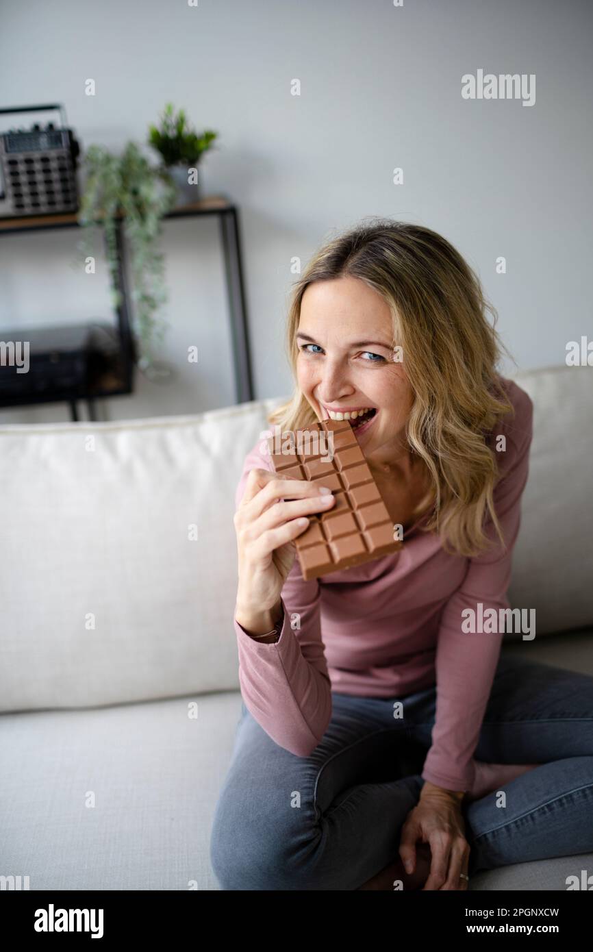 Glückliche Frau, die zu Hause Schokolade auf dem Sofa isst Stockfoto