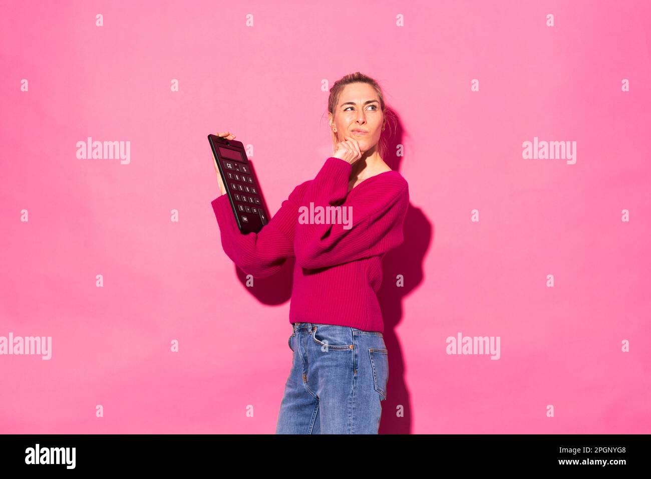 Verwirrte Frau mit Taschenrechner vor pinkfarbenem Hintergrund Stockfoto