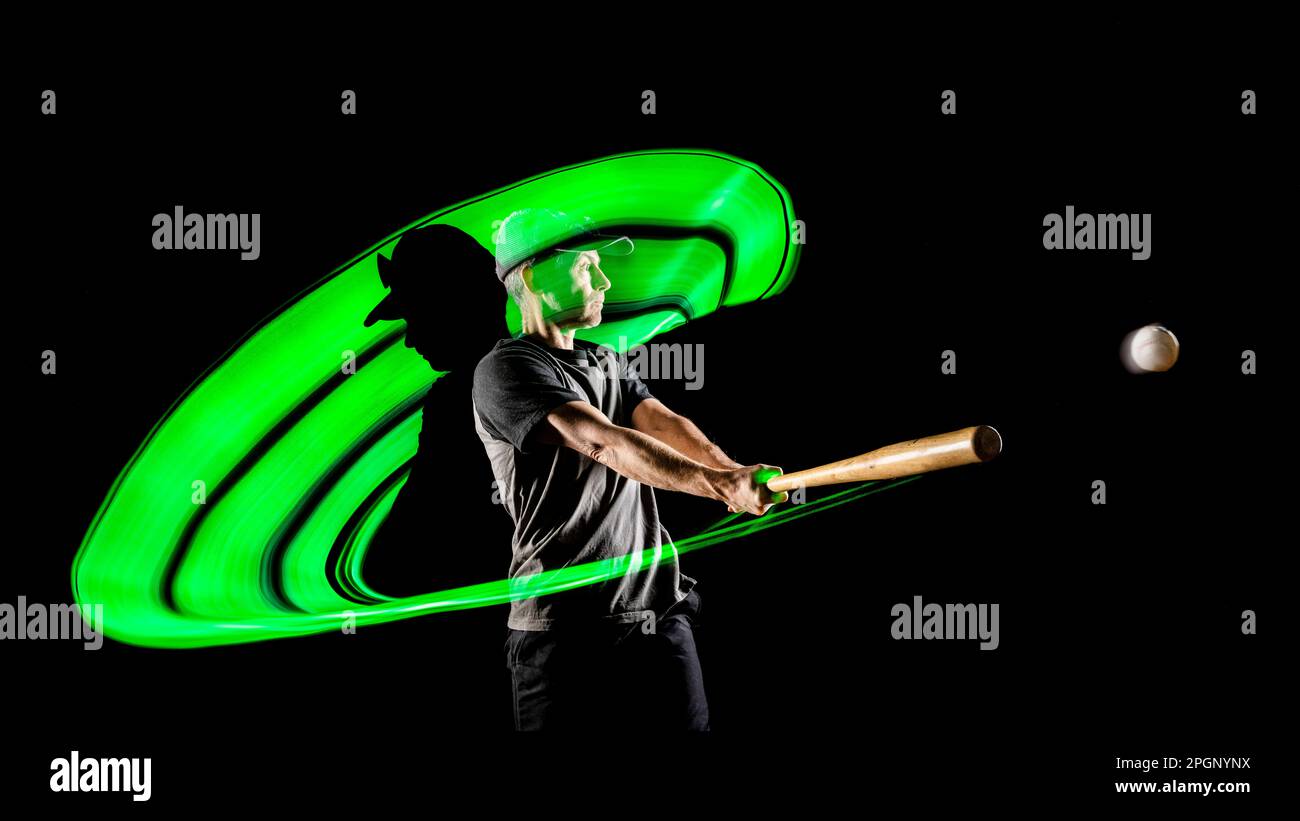 Sportler schlägt Ball mit Baseballschläger vor schwarzem Hintergrund Stockfoto