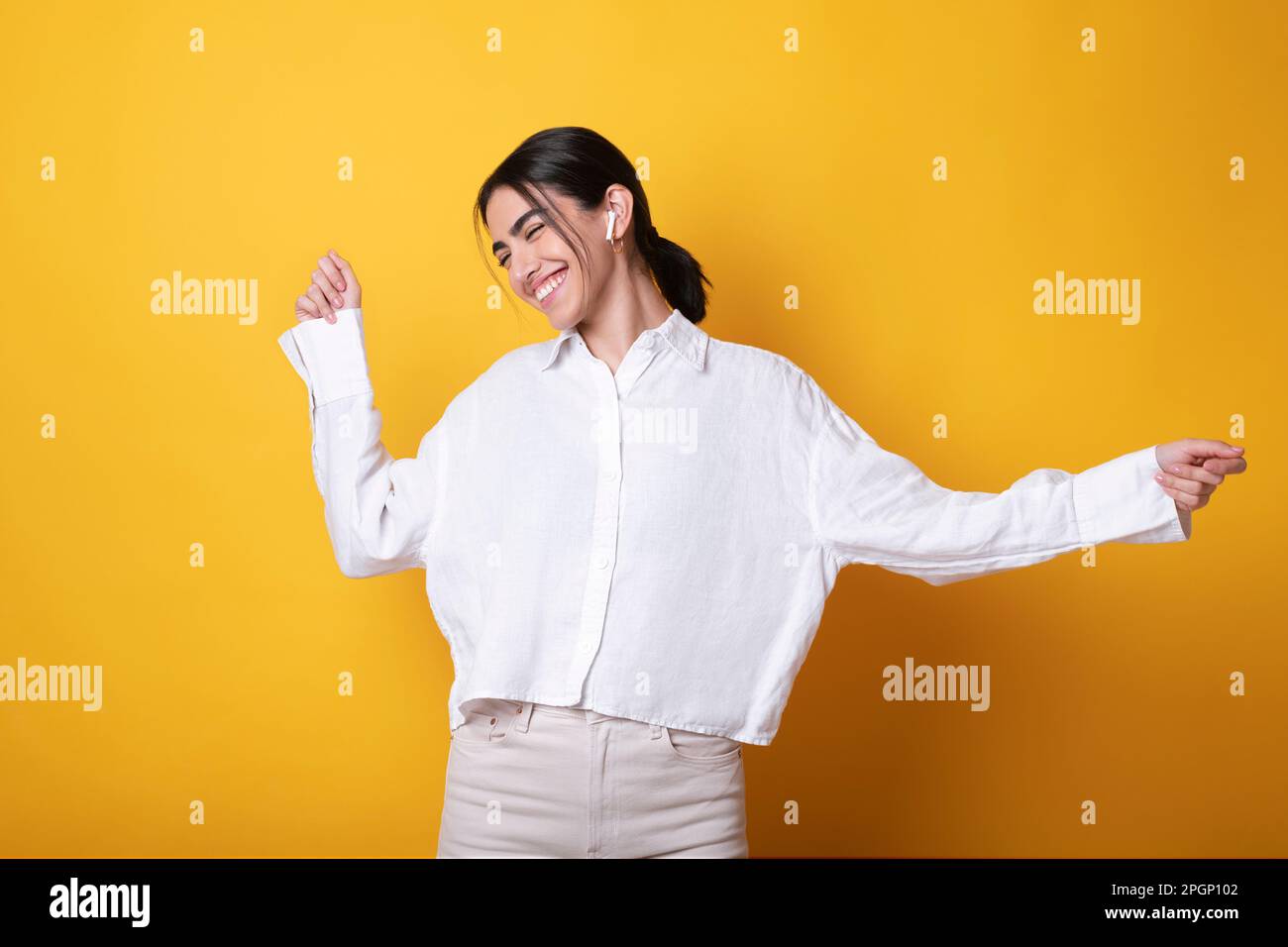 Glückliche Frau mit kabellosen in-Ear-Kopfhörern, die Musik hört und vor gelbem Hintergrund tanzt Stockfoto