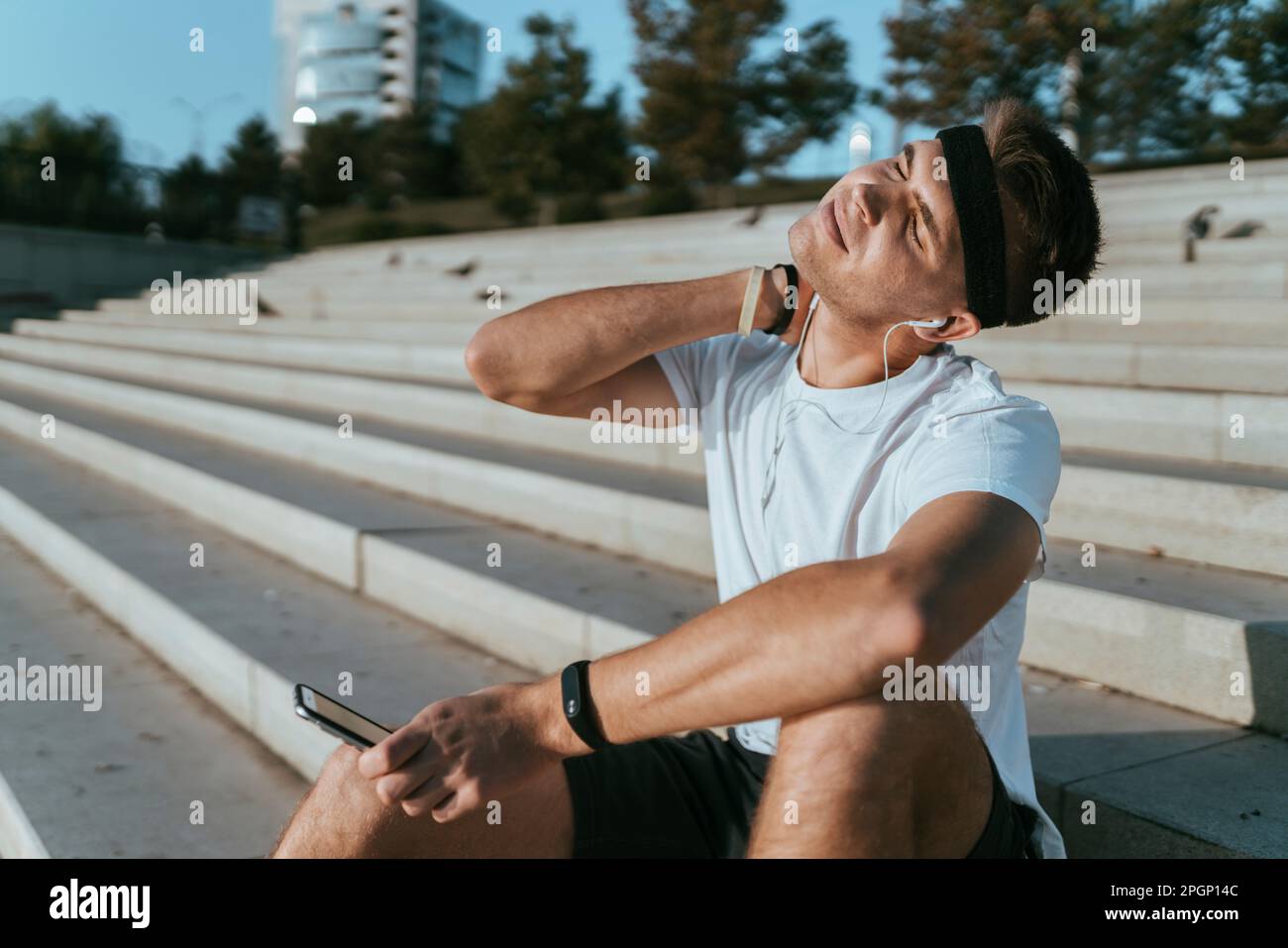 Junger Mann, der sich den Hals streckt und auf Treppen sitzt Stockfoto