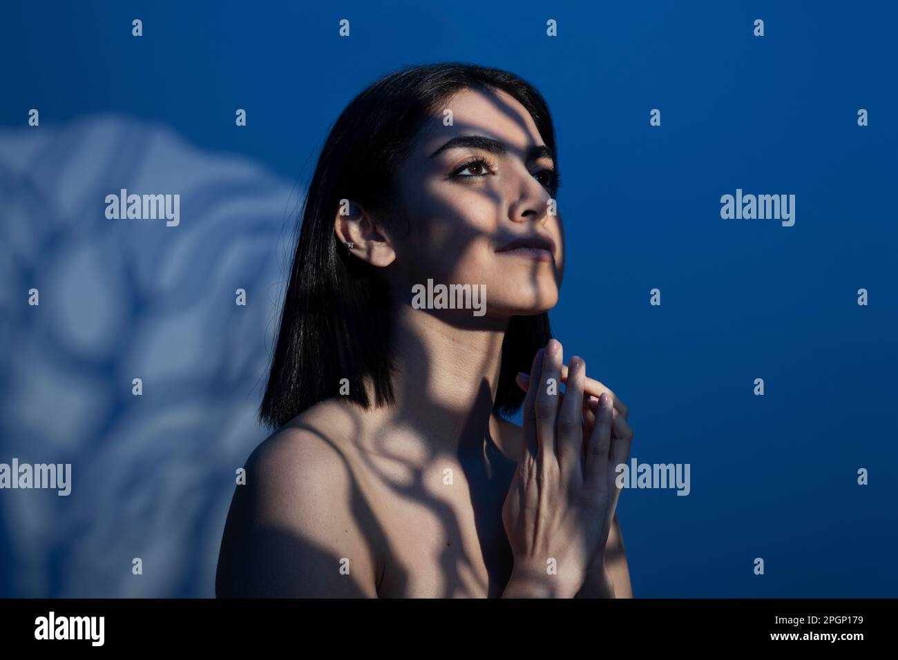 Aufmerksame junge Frau mit Licht im Gesicht vor blauem Hintergrund Stockfoto