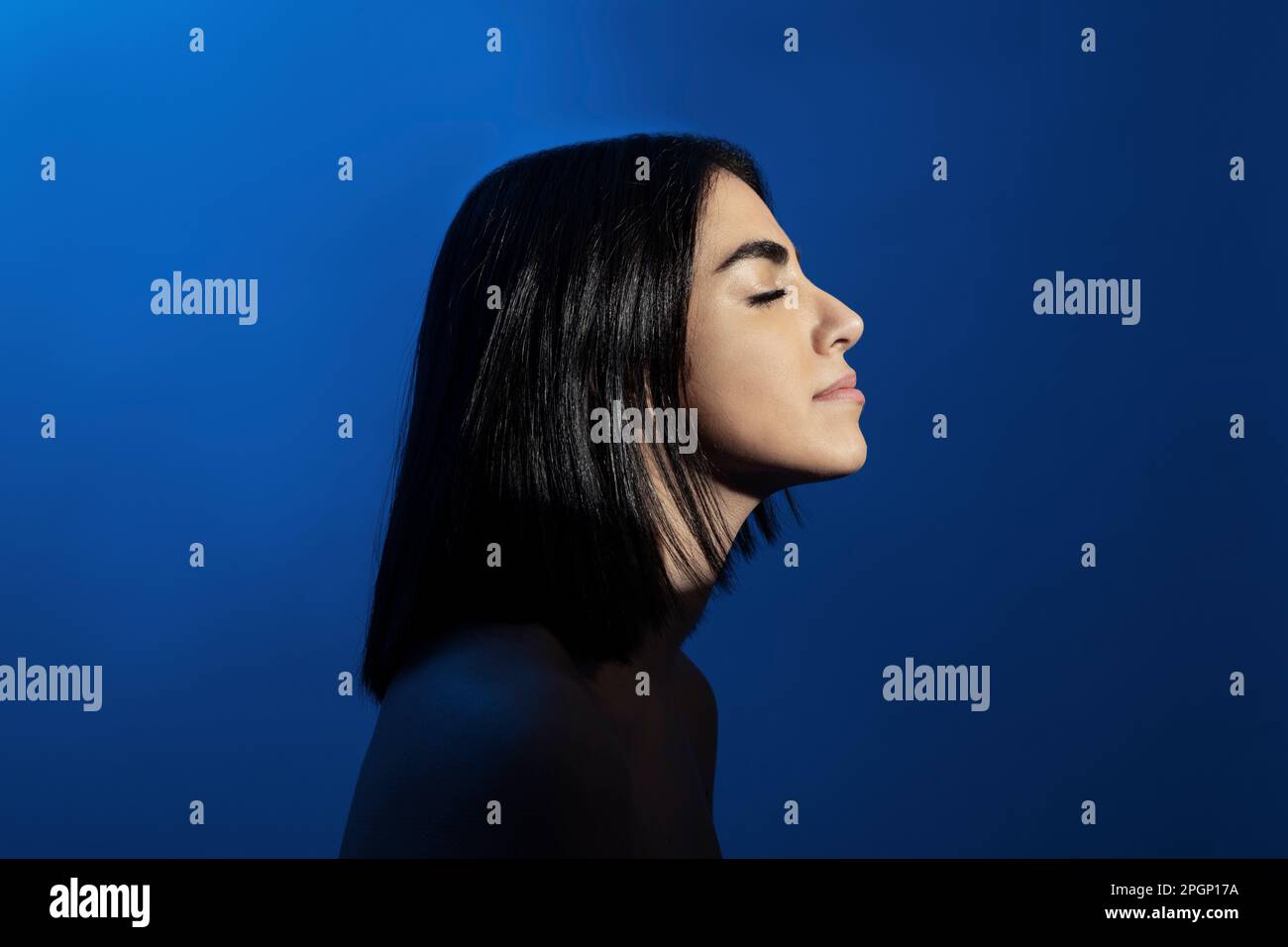 Junge Frau mit geschlossenen Augen vor blauem Hintergrund Stockfoto