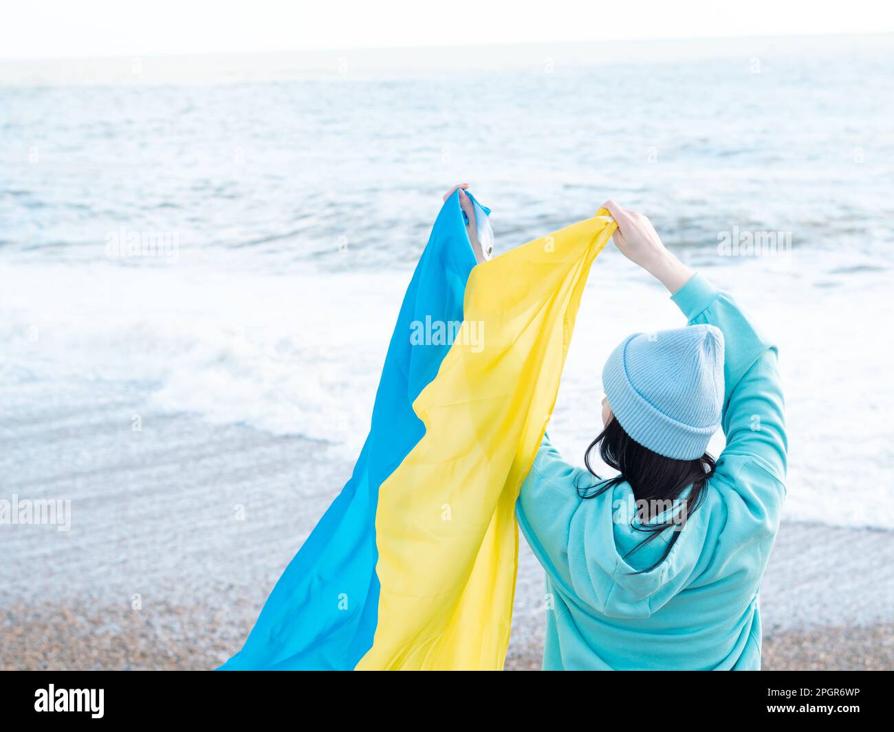 Braune Frau in blauem Hoodie und blauem Hut mit ukrainischer Nationalflagge, patriotisches Konzept Stockfoto