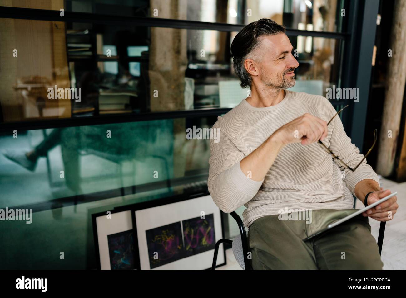 Weißer Mann mittleren Alters, der einen Tablet-Computer benutzt, während er im modernen Büro drinnen sitzt Stockfoto