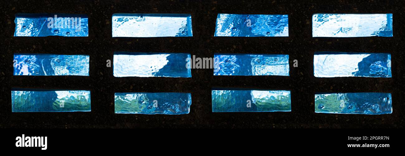 Rechteckige Glassteine mit abstraktem blaugrünem Muster in einer dunklen Steinwand Stockfoto
