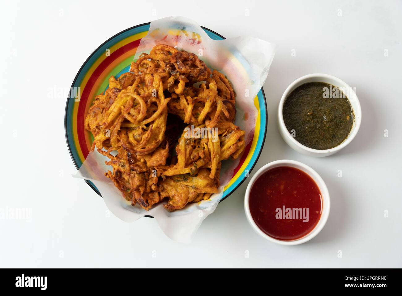 Gebratene Zwiebelpakora, beliebter indisch-pakistanischer Teezeit-Snack während der Regenzeit. Serviert mit Minze und süßen Chilisaucen auf strukturiertem Hintergrund Stockfoto