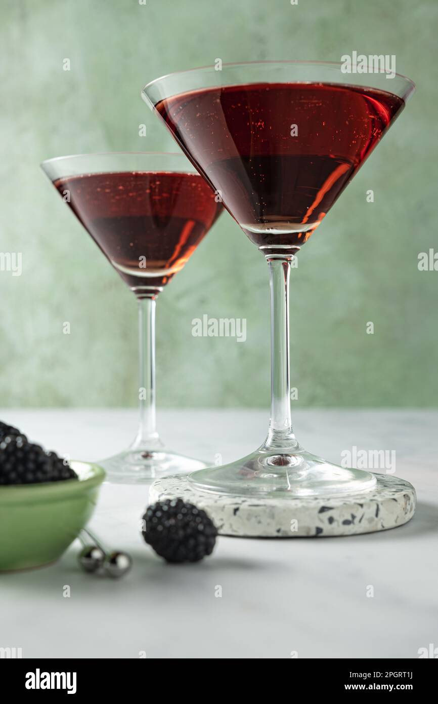 Zwei rote Cocktails (Brombeeren/Himbeeren) in martinigläsern vor hellgrünem Hintergrund. Stockfoto