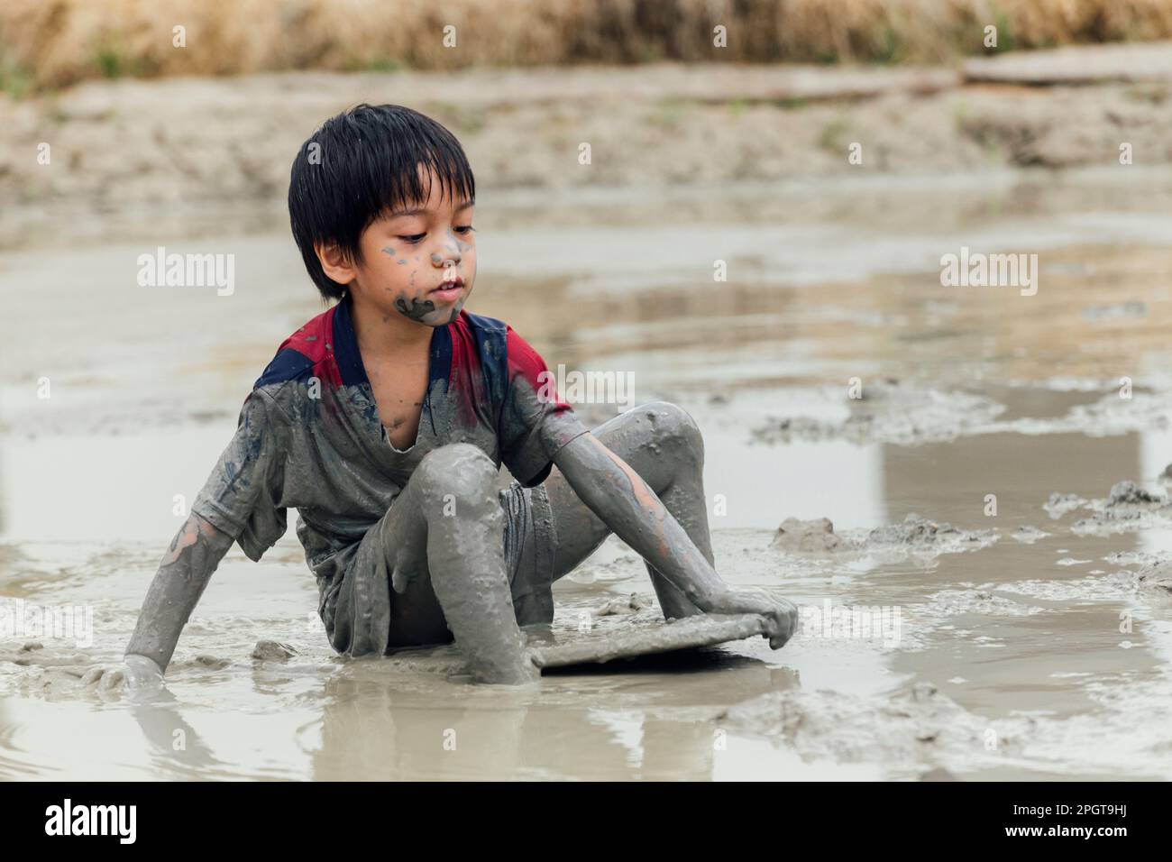 Süßer, glücklicher kleiner asiatischer Junge, der gerne im Schlamm auf dem Spielplatz spielt. Kindererziehung in der Natur an der montessori-Schule. Natur- und Bildungskonzept. Stockfoto