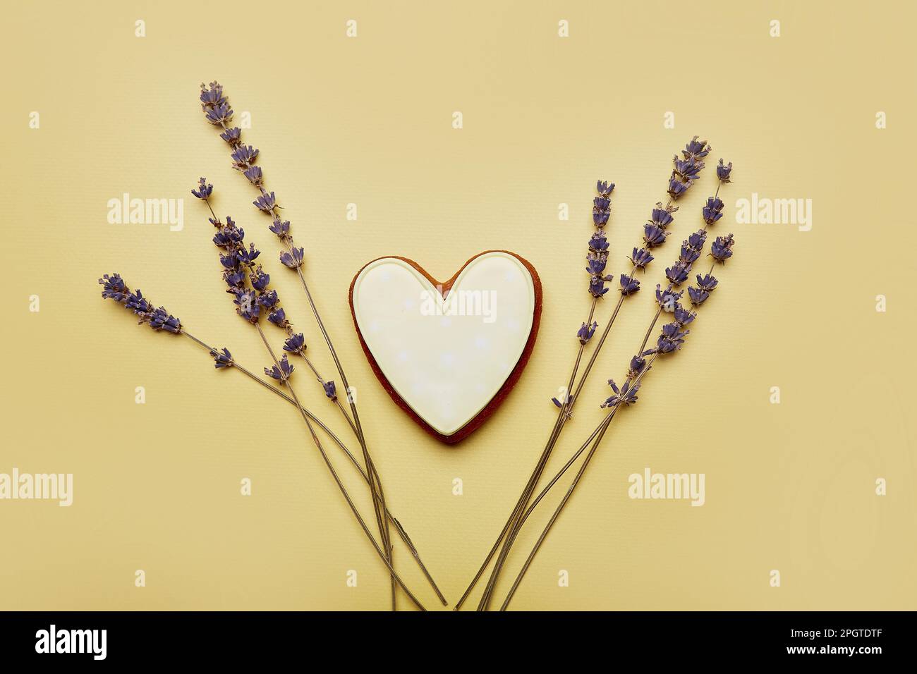 Ästhetischer Keks in Herzform mit Lavendel. Frauentag, Muttertag. Frühlingskarte mit gebackenen, glasierten Keksen auf gelbem Hintergrund. Weiblicher Backg Stockfoto