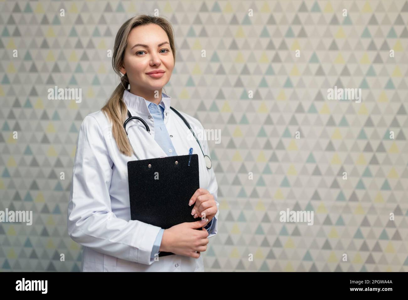 Foto einer attraktiven Hausärztin, die die Patienten berät und freundlich lächelt, weißer Laborkittel und Stethoskop. Stockfoto