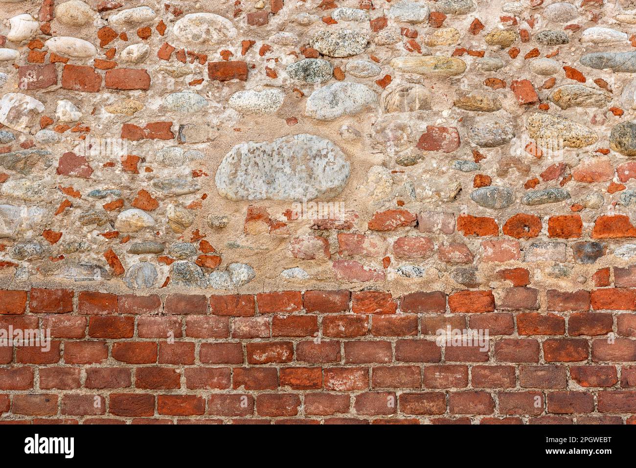 Wandtextur mit regelmäßiger roter Ziegelbasis und über der Wand mit Stücken alter roter Ziegelsteine vermischt mit freiliegenden runden Flusssteinen. Kopierbereich im Hintergrund Stockfoto