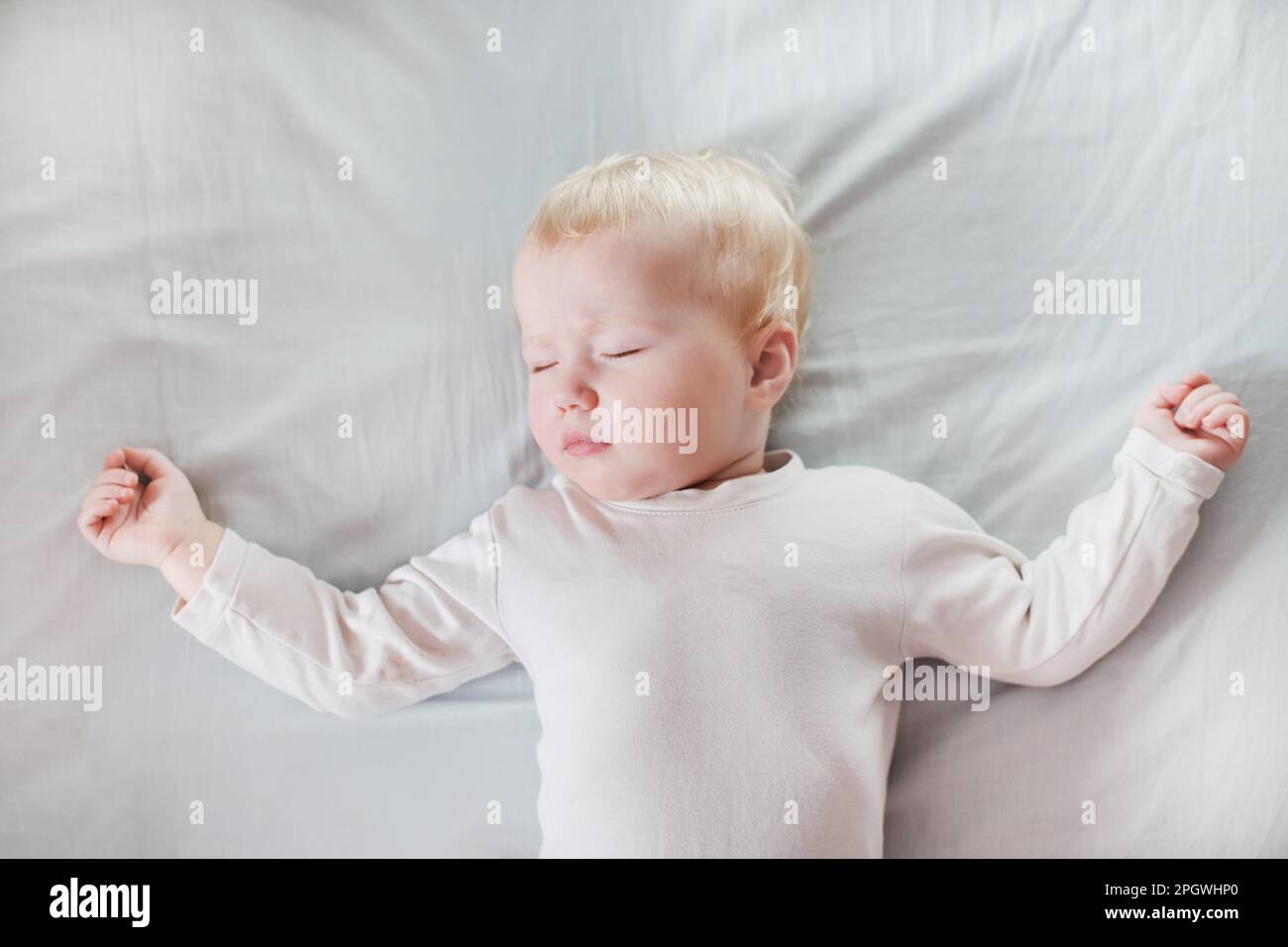 Süßes kleines Mädchen schläft auf weißer Bettwäsche im Bett. Kind 1 Jahre, das die Hände hebt. Glückliche Kindheit und Schlafprobleme bei Kindern Konzept Stockfoto