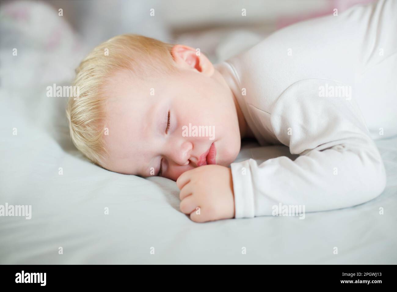 Ein Kind ruht sich tagsüber zu Hause mit einem Stift und einer Faust neben dem Gesicht aus. Das kleine Mädchen schläft auf dem Bauch Stockfoto
