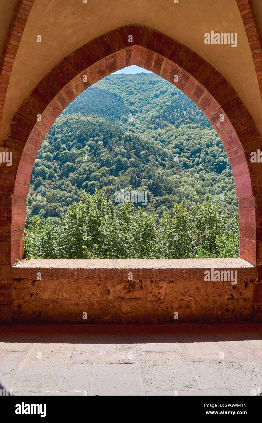 Fenster in den Gewölben einer Bergabtei mit grünem Wald im Hintergrund Stockfoto