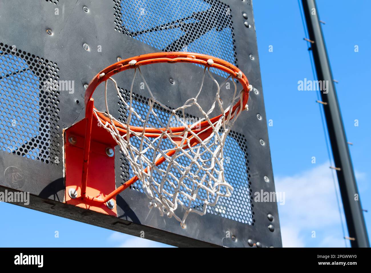 Öffentlicher Basketballkorb im Stadtpark mit schwarzer industrieller Metallrückwand und sonnenblauem Himmel Stockfoto