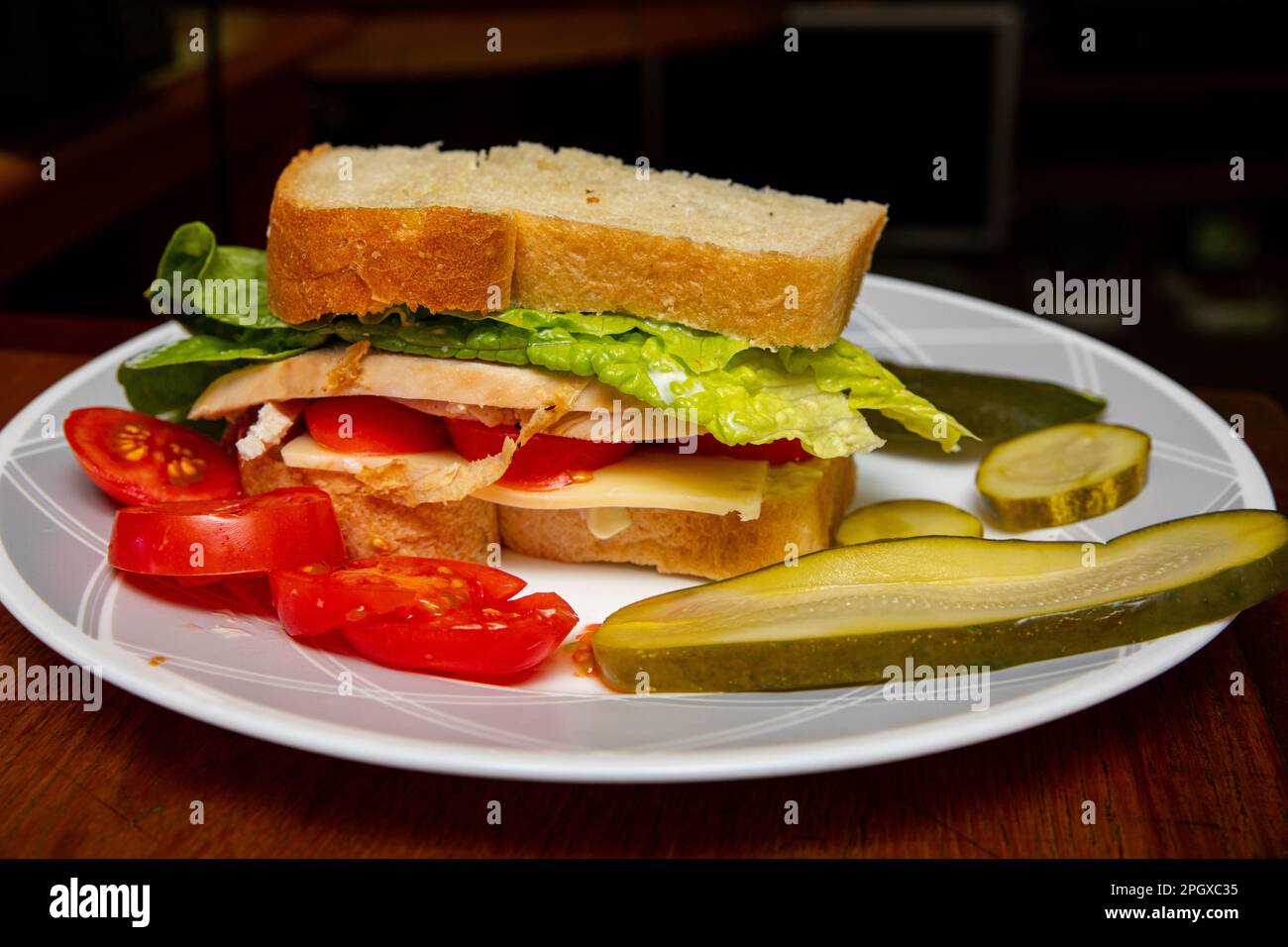 Ein Sandwich mit geröstetem Hühnchen auf dem Hausmannskost Brot mit Romaine, Schweizer Tomaten und Mayonnaise mit hausgemachten Dill-Gurken und Tomatenscheiben auf der Seite Stockfoto