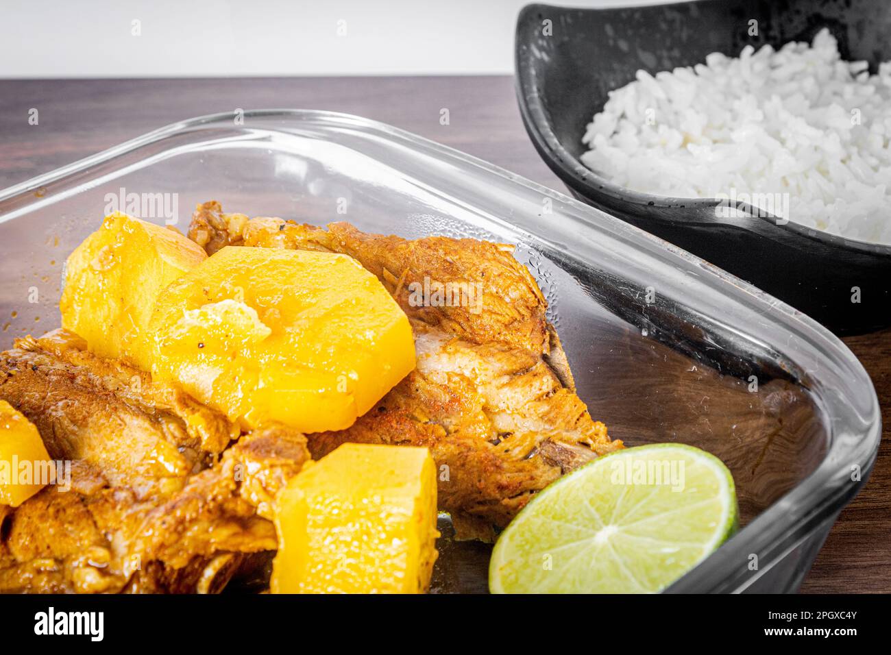 Schweinerippchen, gekocht in einem Schnellkocher auf einem Holztisch. Weißes Handtuch um die Schüssel. Reis und ein Holzlöffel. Ansicht schließen. Stockfoto