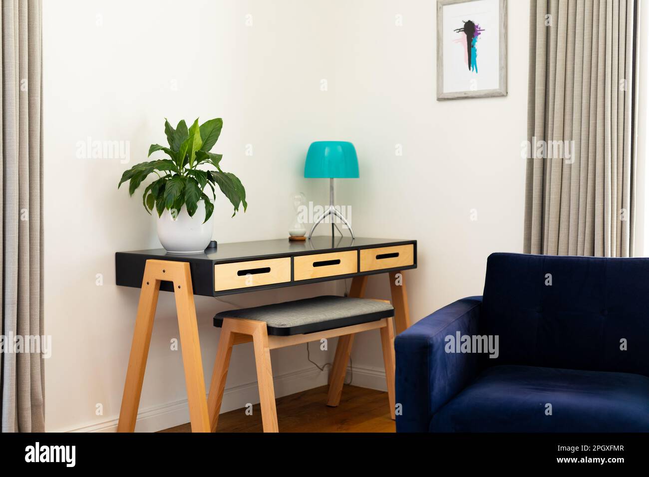 Wohnzimmerecke mit Sessel, Pflanze und Lampe auf Tisch, Vorhängen und Wandgemälden Stockfoto
