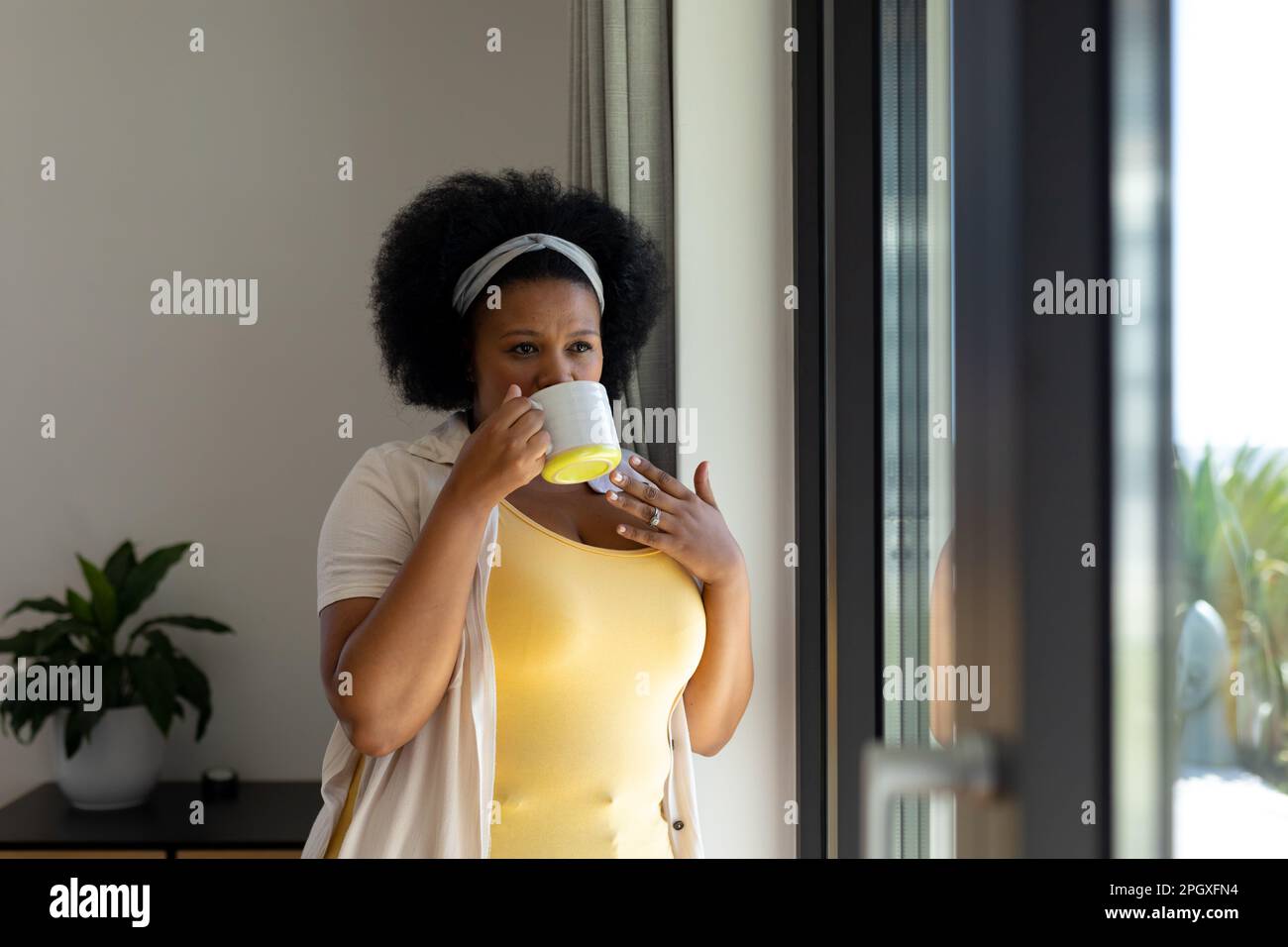 Eine fürsorgliche afroamerikanerin in Übergröße, die aus dem Fenster schaut und Kaffee trinkt Stockfoto