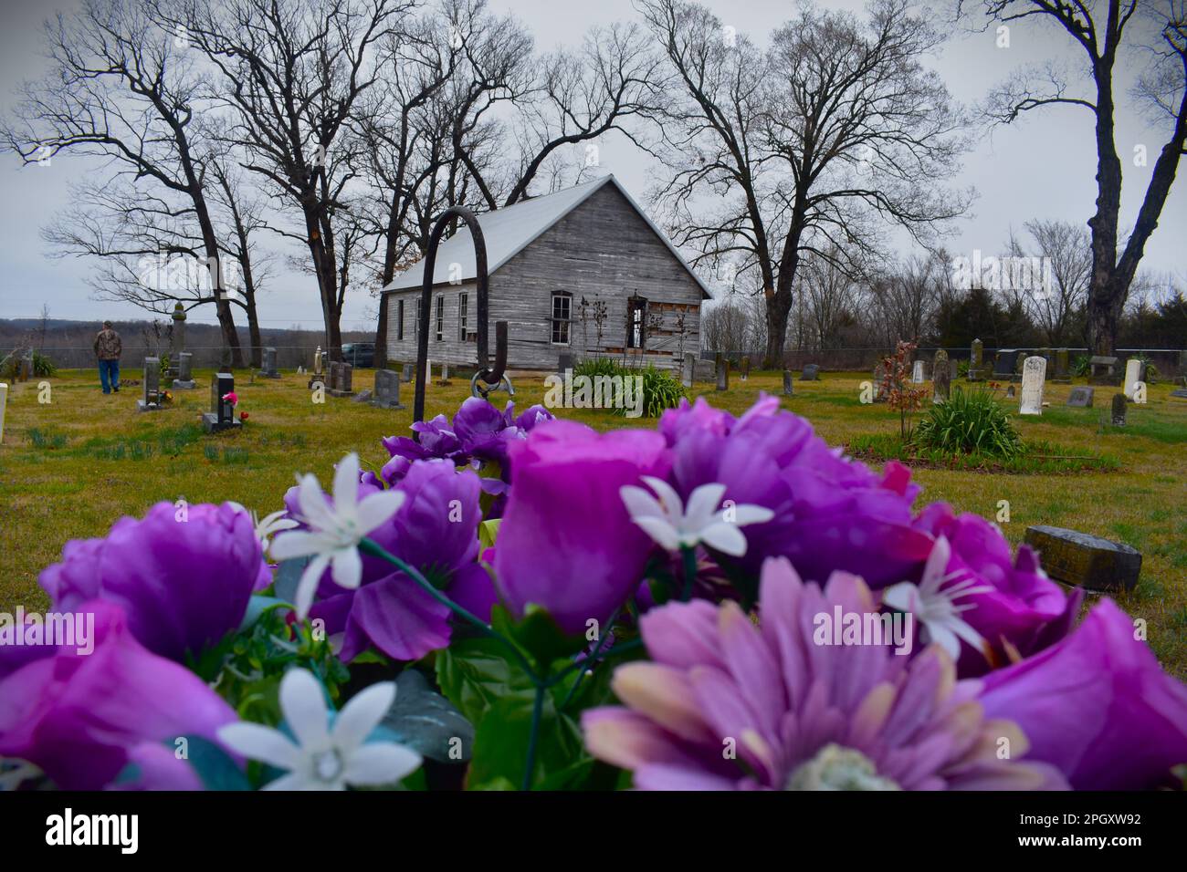Nahaufnahme von Blumen auf einem Grabstein, mit einer alten, verlassenen Landkirche im Hintergrund. Ländliche Missouri, MO, USA, USA Stockfoto