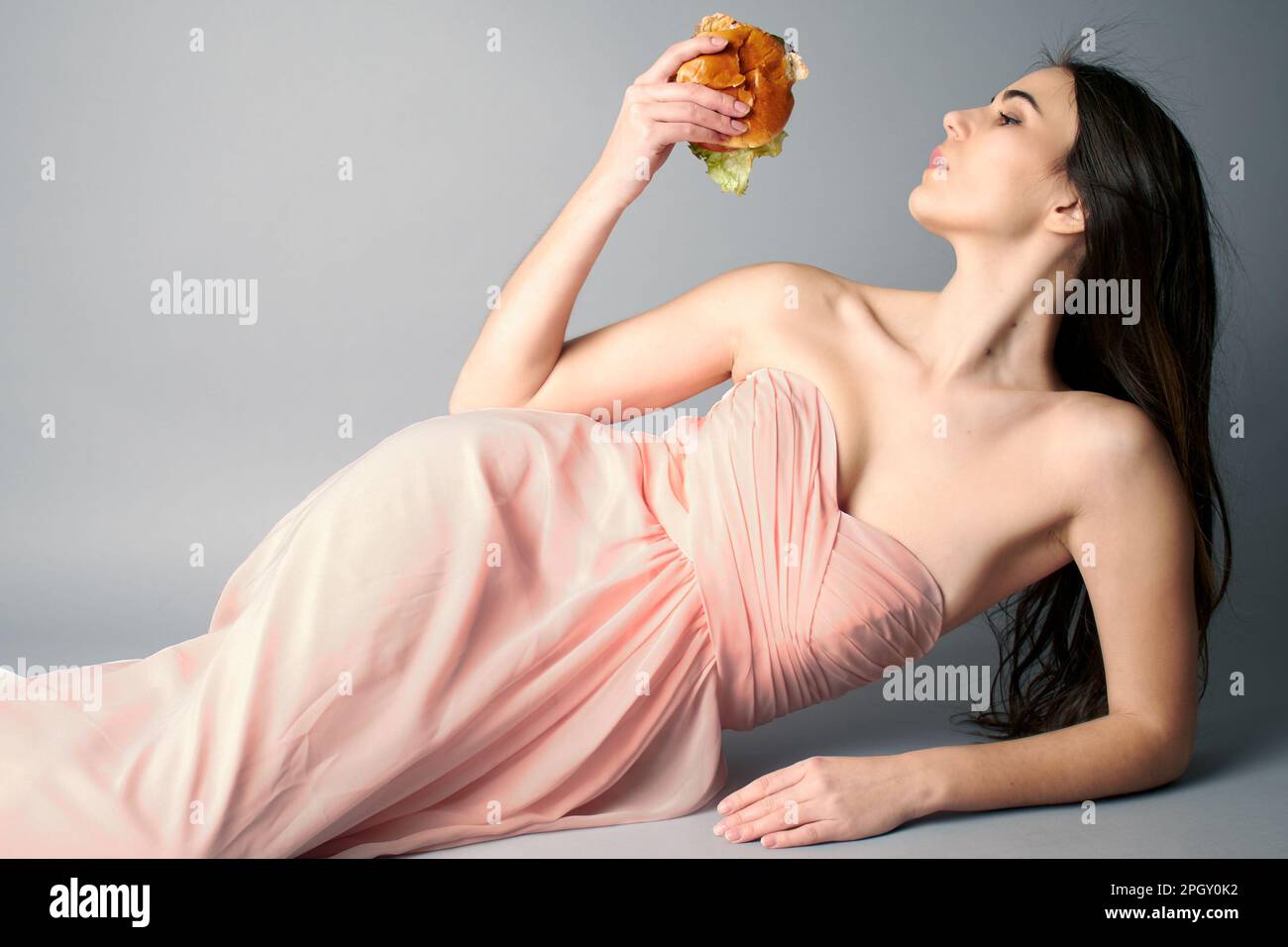 Eine Frau, die in einem durchgehenden pinkfarbenen Ballkleid mit einem Hamburger lag Stockfoto