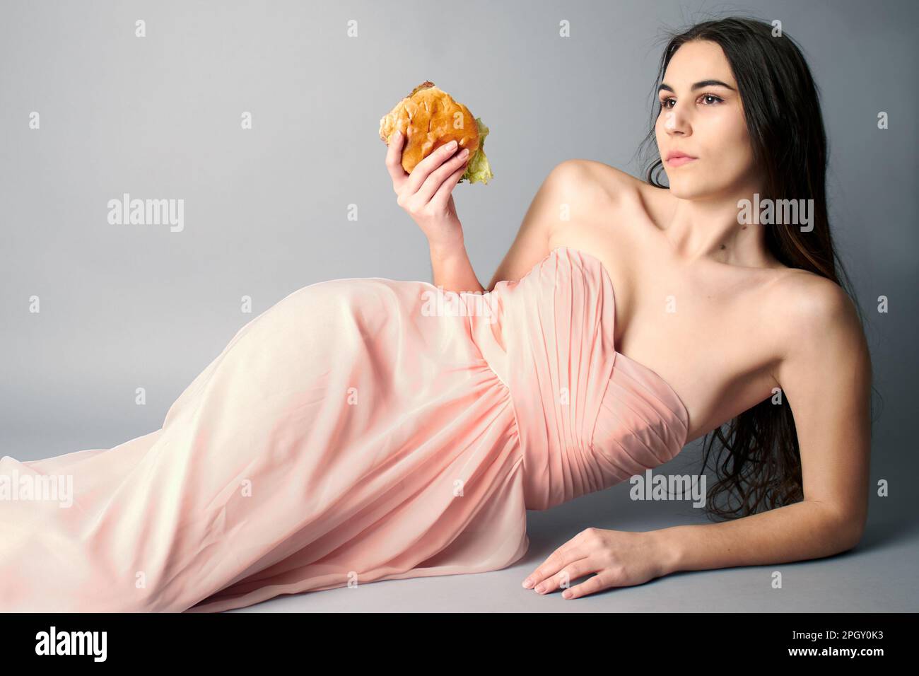 Porträt einer Frau, die mit Hamburger-Cheeseburger auf dem Boden liegt Stockfoto
