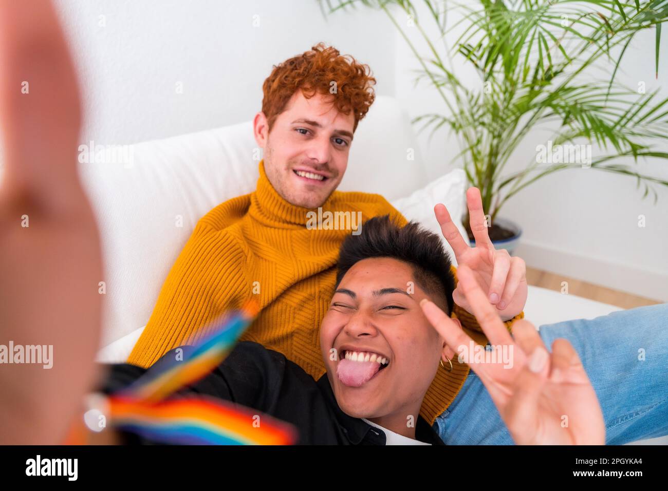 Wunderschönes schwules Paar, das zu Hause romantisch ist, auf dem Sofa, schwules Paar, das Selfie macht und Siegeszeichen macht, lgbt-Konzept Stockfoto