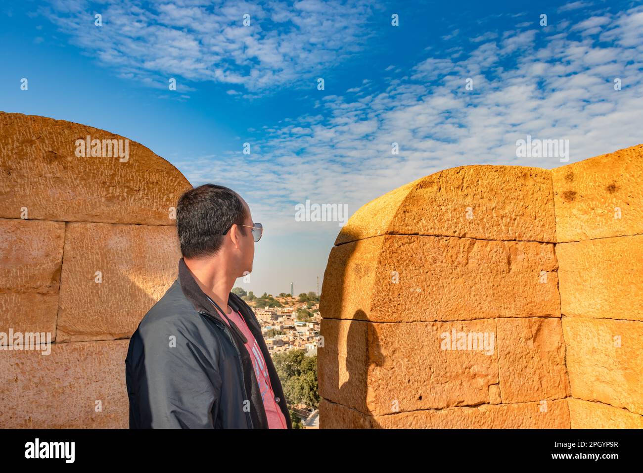 Mann, der tagsüber die architektonische Aussicht auf die Wüstenstadt mit hellblauem Himmel von der Festung jaisalmer aus beobachtet Stockfoto