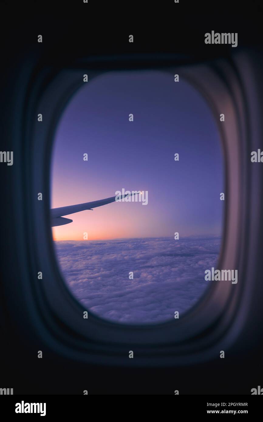 Blick aus dem Fenster des Flugzeugs während des Fluges über den Wolken bei Sonnenaufgang. Selektiver Schwerpunkt auf Flugzeugflügel. Stockfoto