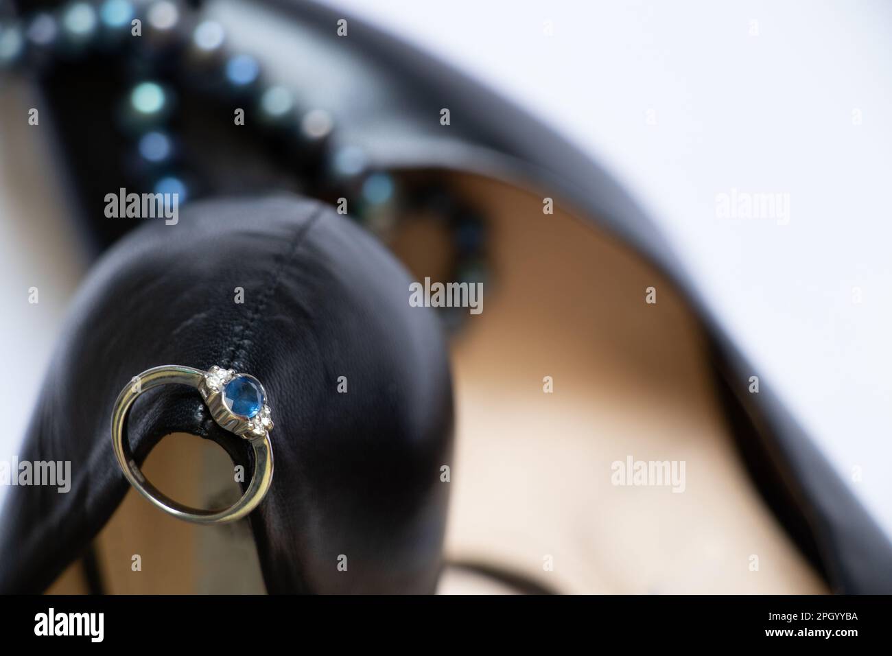 Schwarze Lederschuhe, weißer Goldring mit Diamanten und Perlen auf weißem Hintergrund Stockfoto