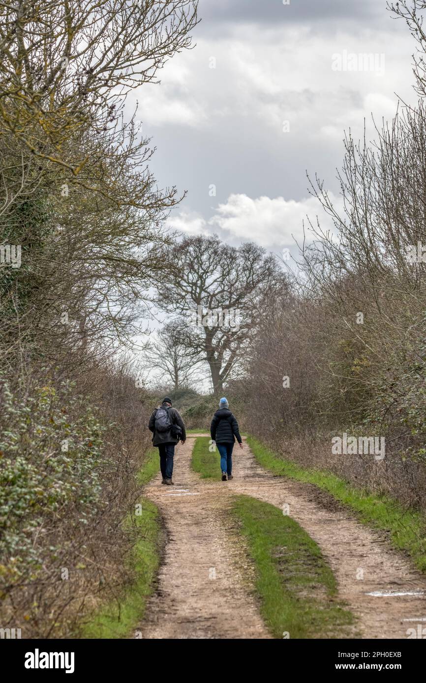 Ein Paar, das Anfang Frühling auf einer Norfolk-Landstraße spaziert. Teil des Snettisham Circular Walk. Stockfoto