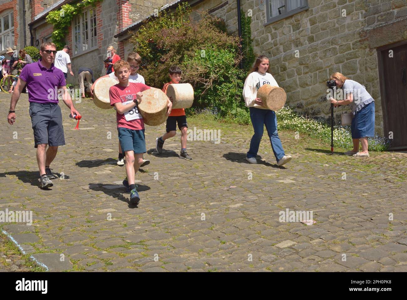 Vier Kinder tragen ihre „Käsesorten“ während des Food and Drink Festivals der Stadt bis zur Startlinie des Käserennens auf dem Gold Hill, Shaftesbury. Stockfoto