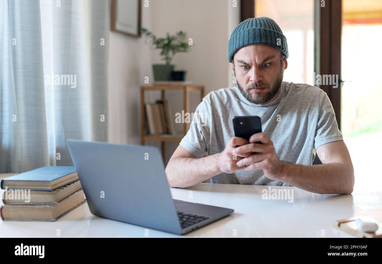 Überraschter Mann mit weit geöffneten Augen, der auf den Bildschirm des Mobiltelefons schaut. Stockfoto