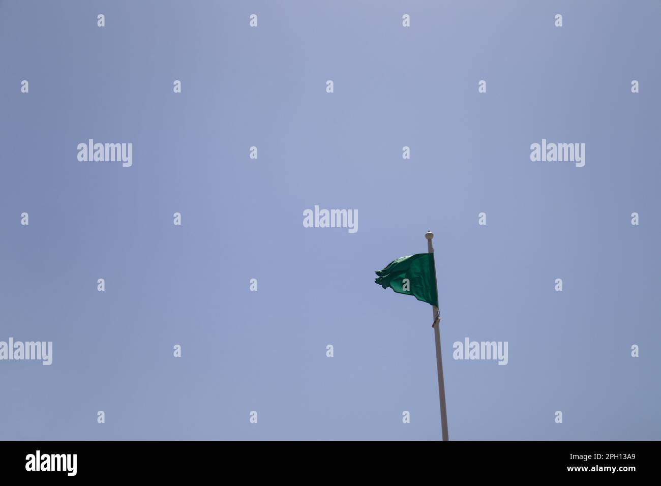 Nahaufnahme einer grünen Flagge an einem Strand mit Silhouette vor dem blauen Sommerhimmel, die symbolisiert, dass das Meerwasser zum Baden geeignet ist Stockfoto