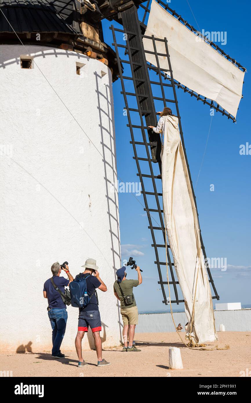 Campo de Criptana, Spanien - 22. Juni 2022: Windmühle mit Mann, der auf die Klingen klettert, um das Tuch zu montieren, damit es funktioniert, und Fotografen und Video ma Stockfoto